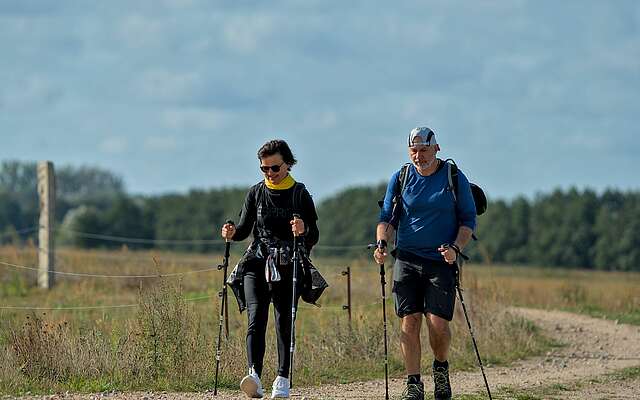 <p>Eine Frau und ein Mann wandern mit Wanderstöcken über einen Feldweg.</p>