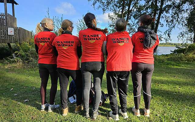 <p>Fünf Frauen stehen mit dem Rücken zum Fotografen. Die Rückseiten ihrer T-Shirts tragen den Aufdruck "WanderWoman".</p>